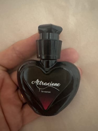 Reviewer's hand holding a small heart-shaped black Attracione perfume bottle.