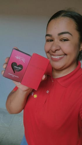 Reviewer sorridente segurando a embalagem vermelha do perfume Attracione Men.