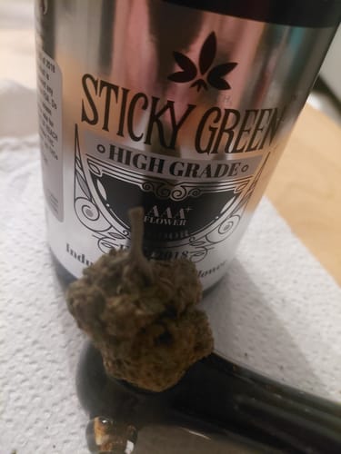 Customer's Silver Haze flower nugget resting in a bowl, positioned in front of a Sticky Green jar.
