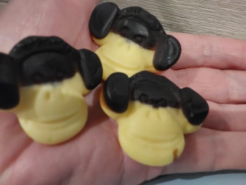 Customer's hand holding three banana-shaped and liquorice-eared soft foam sweets.