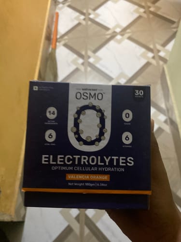 Customer's hand holding a dark blue box of OSMO Electrolytes Valencia Orange sachets.