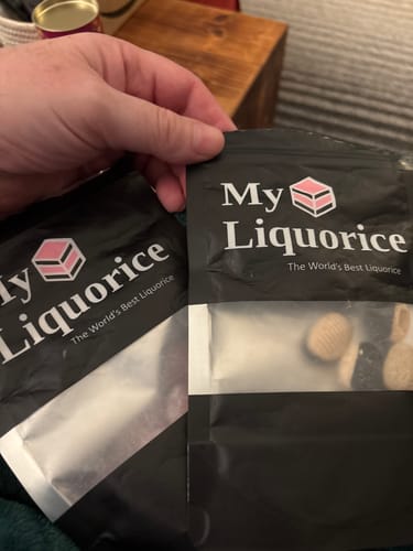 Customer's hand holding two My Liquorice brand bags of Hard Boiled Raspberry & Liquorice sweets.