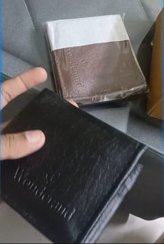 Customer's hand holding a black wallet labeled Wonderland, with another brown wallet in its plastic packaging nearby.