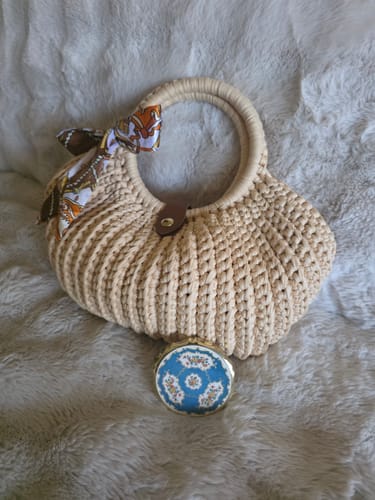 Customer's CrochetPark Shell crochet handbag in beige with a patterned bow, resting on a textured surface.