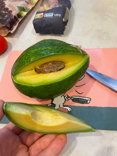 Customer's aufgeschnittene Avocado Hass mit grünem Fruchtfleisch und großem Kern auf einem Schneidebrett.
