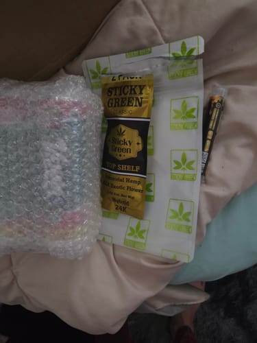 Customer's 24K Hybrid Infused Top Shelf Pre Rolls packaging, featuring a gold pouch with labels, resting on a soft surface.