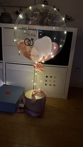 Kunden-Geschenkbox Rund mit leuchtendem Designer-Ballon inklusive Namen und Datum, dekoriert mit kleinen Luftballons.