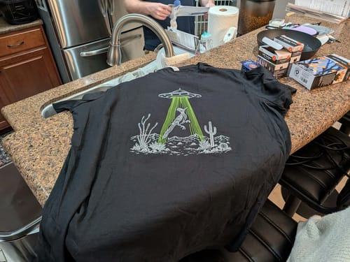 Customer's Roadrunner and UFO Women's Relaxed Tee displayed on a kitchen counter, showing the desert graphic.
