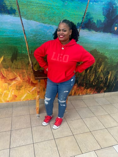 Reviewer wearing a red Zodiac Puff Print Hoodie with LEO text, paired with distressed blue jeans.