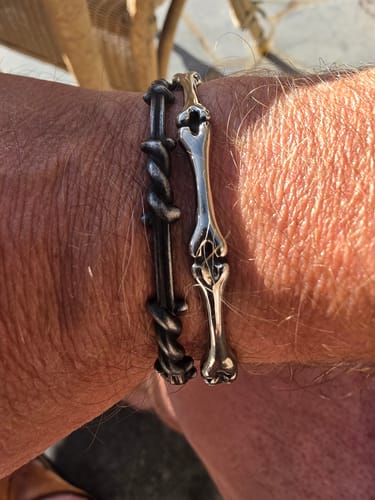 Reviewer's wrist wearing a dark barbed wire WIRED bracelet next to a silver bone-shaped bracelet.