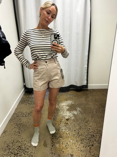 Customer's Tinnie Shorts in stone color, worn with a striped long-sleeve shirt in a dressing room mirror selfie.
