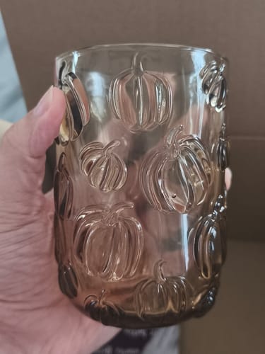 Customer's Hand hält das getönte Trinkglas mit Kürbisrelief vor neutralem Hintergrund