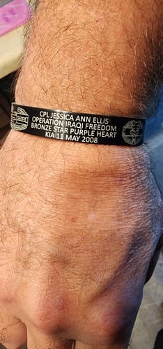 Customer's black personalized memorial bracelet worn on their wrist, showing engraved text and military badges.