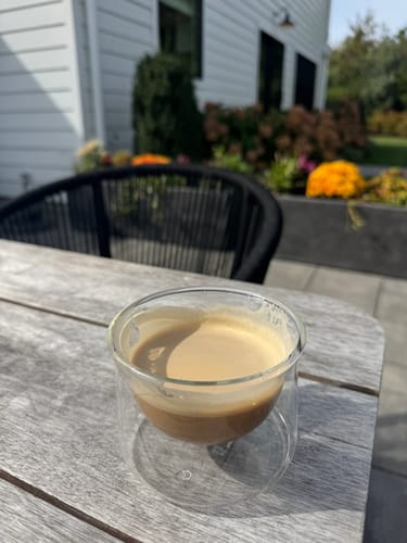 Customer's FLUR Espresso Glass filled with coffee on a wooden patio table outdoors.