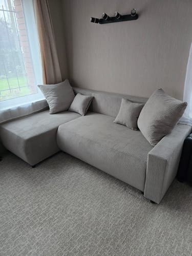 Customer's POLO sofa in light grey, placed in a corner by a window in a living room.