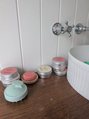 Reviewer's Jasmine & Cypress Shampoo Bars in metal tins and on a wooden dish, sitting on a bathroom vanity.