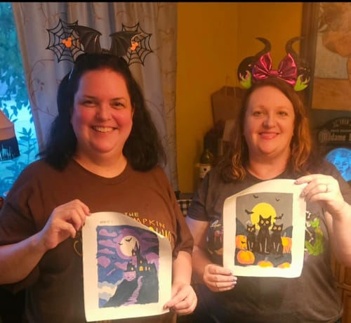 Customer's Spooky Autumn Set mini paintings held by two reviewers, showing completed halloween themes.