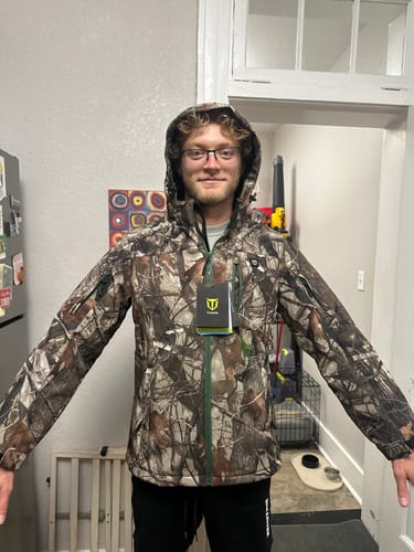 Customer's camo heated jacket with hood up, showing the fit on a person, with a product tag attached.