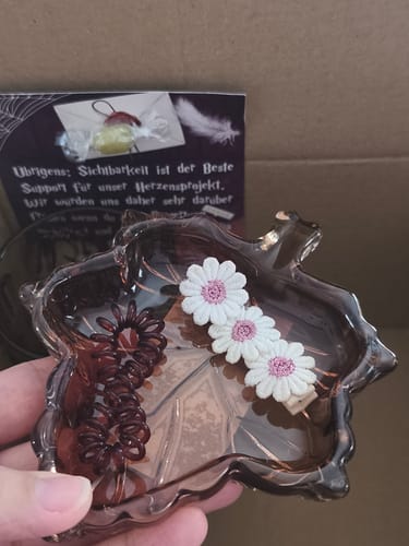 Reviewer's braune Ahornblatt-Schmuckschale aus Glas, gehalten in der Hand mit Haarschmuck darin.