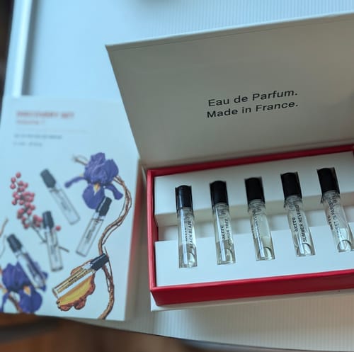 Customer's Discovery Set Volume 1 with five perfume vials inside an open box, next to the illustrated product packaging.