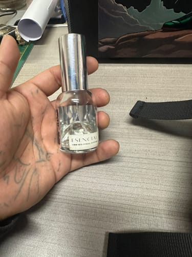 Customer's hand holding a small glass bottle of H506 perfume against a desk background.