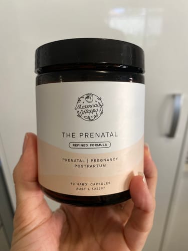 Reviewer's hand holding The Prenatal brown capsule bottle with white label.