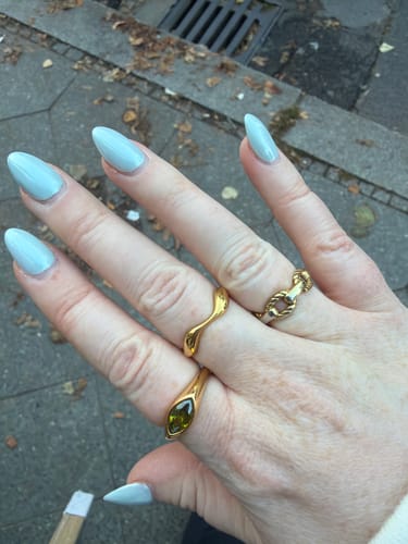 Reviewer's 18K Gold Wave Ring worn on a finger with two other gold rings, featuring a hand with light blue nails.