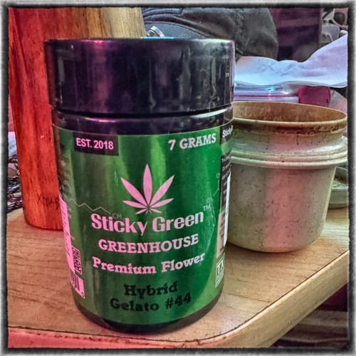Customer's green Gelato 44 THCA flower jar sitting on a wooden surface next to an empty bowl.