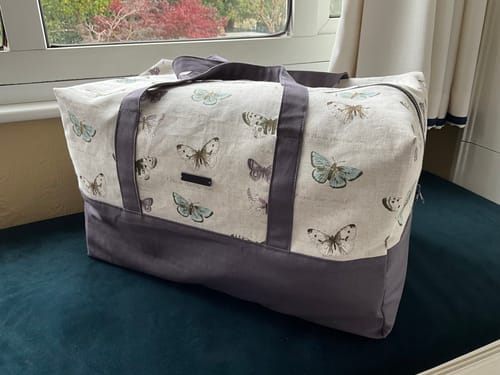 Customer's weekend bag made from Butterflies on Mottled Cotton Canvas Fabric, sitting on a teal bench.