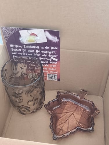 Customer's packaging for products, including a dark glass candle holder and leaf-shaped dish with an included note card.