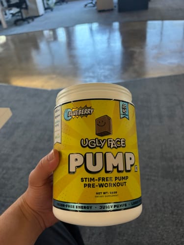 Customer's hand holding a yellow tub of UGLYFACE PUMP V2 pre-workout supplement.