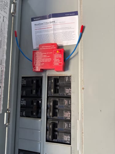 Customer's red NovaCare Fire Guard mounted inside a grey electrical breaker panel with its paper manual.