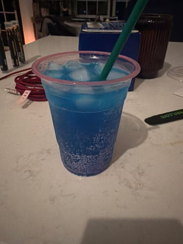 Customer's blue, ice-filled 100MG Infused Soda THC Infused in a plastic cup with a green straw.