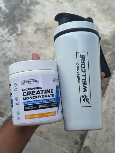 Customer's hand holding a Wellcore Micronised Creatine Monohydrate tub and a white stainless steel shaker.