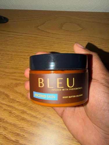 Customer's hand holding a brown jar of Bleu Body Butter Cologne with a black lid.