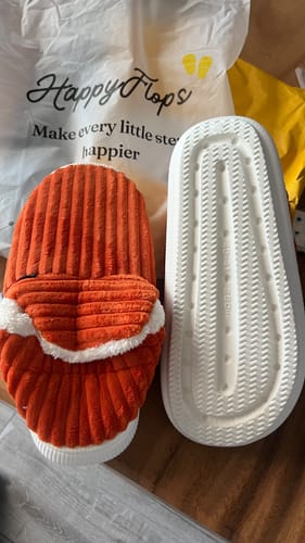 Customer's HappyCozy slippers showing a textured orange upper and a white grooved sole next to the brand packaging.