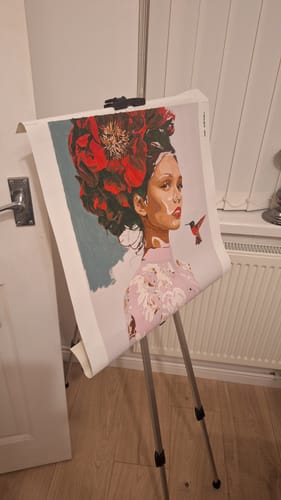 Customer's Scarlet Blossom Muse paint by number on an easel, featuring a woman with a large red flower and a hummingbird.