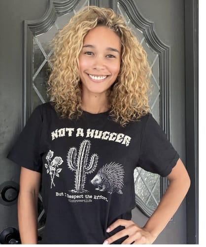 Customer's Not A Hugger Introvert T-Shirt, a black shirt with cactus, rose, and porcupine graphic, worn by a smiling person.