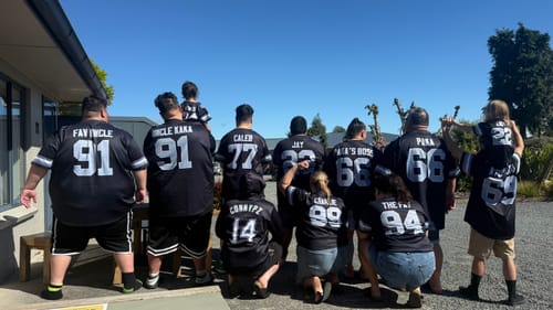 Customer's group of people wearing personalized black American Football Jerseys with names and numbers on back outdoors.