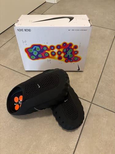 Customer's Nike Mind 001 sneakers in black resting on the floor in front of their product packaging box.