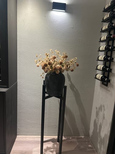 Klant's Wax Arrangement in een zwarte vaas op een zwarte standaard, geplaatst in een sfeervol interieur.