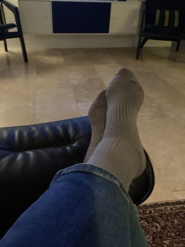 Reviewer's feet wearing grey Diasocks støttestrømper while resting on a dark chair