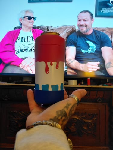 Customer's Rocket Pop Universal Buddy can cooler held in hand in front of a TV screen.
