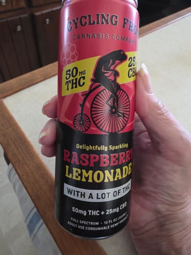 Customer's hand holding a red Sparkling THC Raspberry Lemonade can showing the frog logo and potency details.