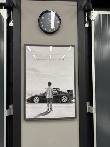 Customer's REMEMBER art print in a black frame, hanging on a gray wall under a round wall clock.