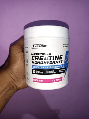 Customer's hand holding a white tub of Wellcore Pure Micronised Creatine Monohydrate Fruit Fusion.