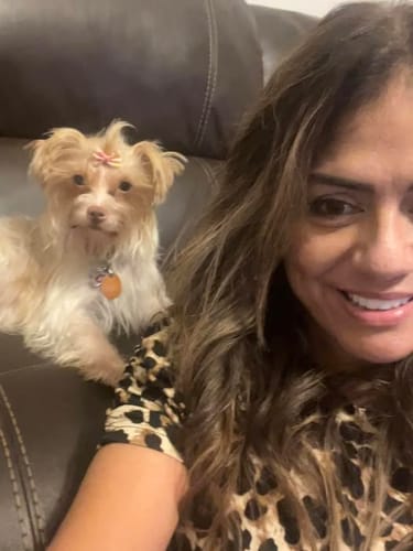 Customer's small light-haired dog with a bow, posing next to a smiling person.