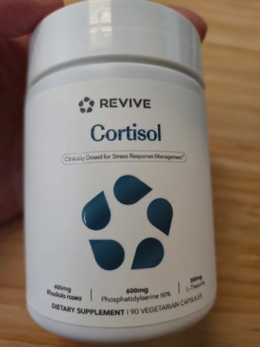 Customer's hand holding a white bottle of Revive Cortisol Support supplement against a wooden surface.