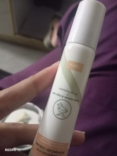 Customer's hand holding the white and beige Advance Lip Pigmentation Cream tube against a blurred background.