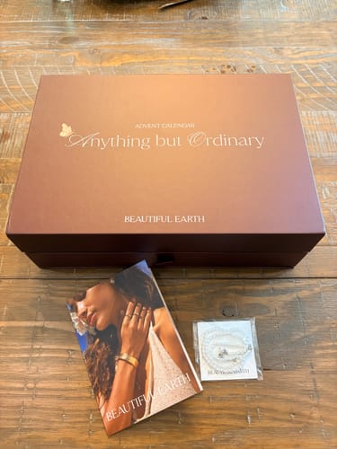 Customer's Advent Calendar box with a pamphlet and a small, wrapped jewelry item on a wooden table.